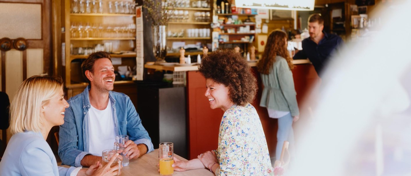 Drei Personen sitzen lachend an einem Tisch in einer gemütlichen Bar. Im Hintergrund sind Gläser und Flaschen zu sehen., © Stuttgart-Marketing GmbH, Alwin Maigler Drei Personen sitzen lachend an einem Tisch in einer gemütlichen Bar. Im Hintergrund sind Gläser und Flaschen zu sehen., © Stuttgart-Marketing GmbH, Alwin Maigler