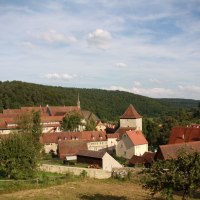 Malerische Stadt mit roten Dächern und Kirchturm, umgeben von grünen Hügeln und Bäumen. Der Himmel ist blau mit einigen Wolken., © Natur.Nah. Schönbuch & Heckengäu Malerische Stadt mit roten Dächern und Kirchturm, umgeben von grünen Hügeln und Bäumen. Der Himmel ist blau mit einigen Wolken., © Natur.Nah. Schönbuch & Heckengäu