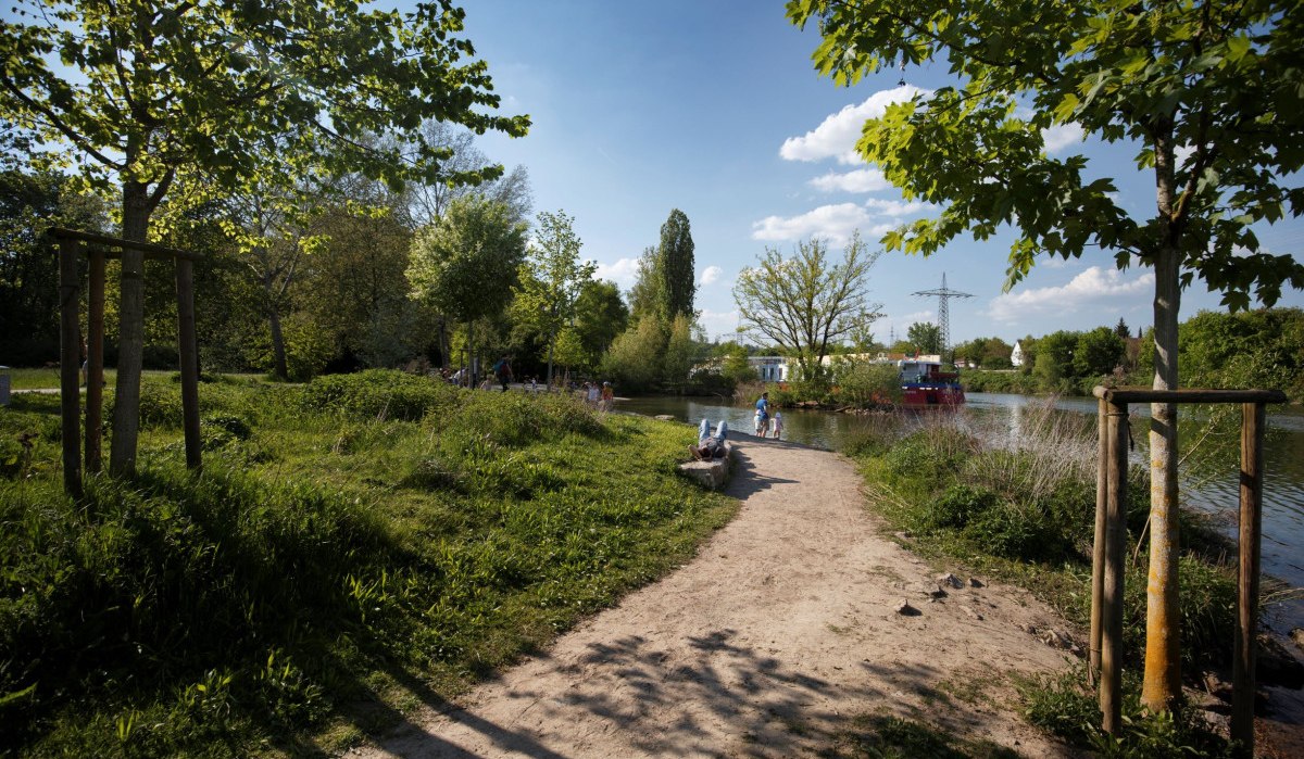 Ein sonniger Weg am Flussufer mit Bäumen und Spaziergängern. Der Himmel ist blau mit Wolken., © Stoppel Ein sonniger Weg am Flussufer mit Bäumen und Spaziergängern. Der Himmel ist blau mit Wolken., © Stoppel