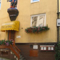Gelbes Gebäude mit dem Schild 'Hotel Wirt am Berg'. Über dem Eingang eine Figur, Blumenkästen an den Fenstern. Rechts ein weiteres Schild mit Hotelnamen., © Hotel Wirt am Berg