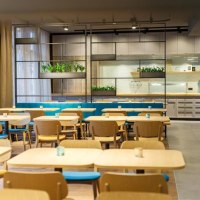 Moderner Speisesaal mit Holztischen und blauen Stühlen. Im Hintergrund sind Pflanzen und Regale zu sehen. Helle, einladende Atmosphäre., © Arthotel ANA Momentum