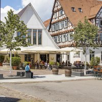 Fachwerkhäuser in Kirchheim unter Teck mit Straßencafé und Bäumen. Menschen sitzen draußen, genießen das Wetter. Historische Architektur und gemütliche Atmosphäre., © Torsten Wenzler