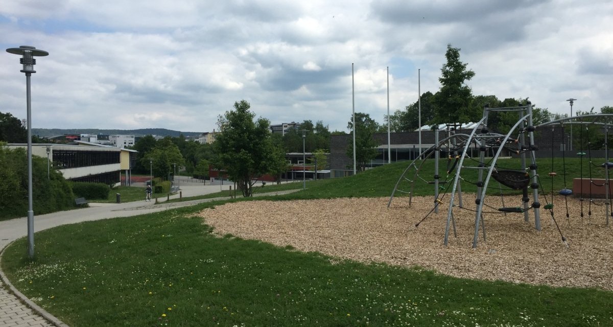 Ein moderner Spielplatz mit Klettergerüst auf einer Grünfläche, umgeben von Gebäuden und Gehwegen unter bewölktem Himmel., © Natur.Nah. Schönbuch & Heckengäu Ein moderner Spielplatz mit Klettergerüst auf einer Grünfläche, umgeben von Gebäuden und Gehwegen unter bewölktem Himmel., © Natur.Nah. Schönbuch & Heckengäu