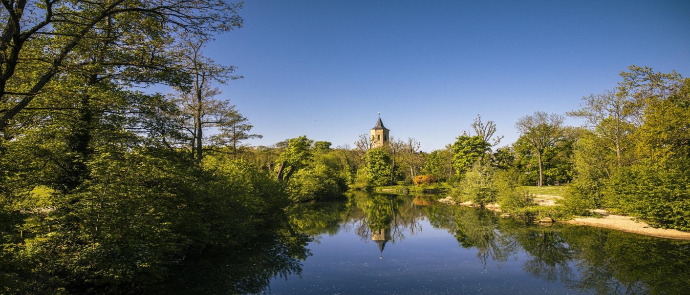 Fluss mit klarem Wasser, umgeben von üppigem Grün. Ein Kirchturm ragt im Hintergrund in den blauen Himmel., © SMG, Sarah Schmid