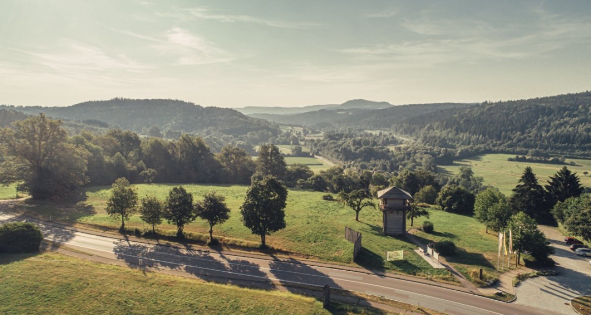 Blick auf eine grüne Landschaft mit einem Limesturm in Lorch, umgeben von Bäumen und Hügeln. Eine Straße verläuft im Vordergrund., © Tourismus Ostalb Blick auf eine grüne Landschaft mit einem Limesturm in Lorch, umgeben von Bäumen und Hügeln. Eine Straße verläuft im Vordergrund., © Tourismus Ostalb