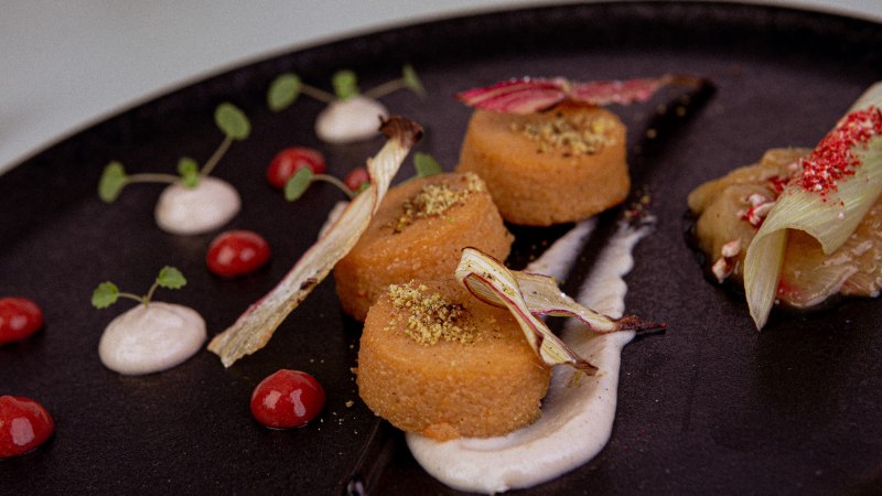 Gourmetgericht auf schwarzem Teller, dekoriert mit Saucen, Kr&auml;utern und Gem&uuml;se. Elegante Anordnung mit verschiedenen Texturen und Farben., &copy; Marc Luppa