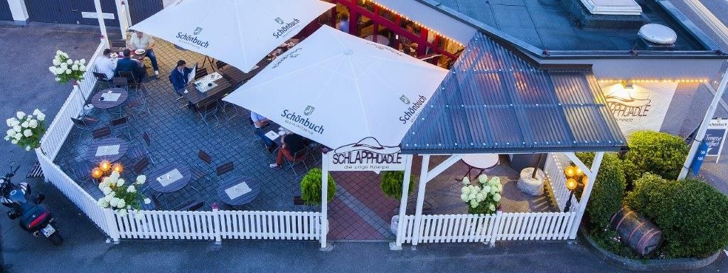 Terrasse mit weißen Sonnenschirmen und Holzmöbeln, umgeben von einem weißen Zaun. Menschen sitzen an Tischen, dekoriert mit Blumen., © Hotel Waldhorn Terrasse mit weißen Sonnenschirmen und Holzmöbeln, umgeben von einem weißen Zaun. Menschen sitzen an Tischen, dekoriert mit Blumen., © Hotel Waldhorn