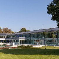 Das Bild zeigt den Außenbereich des Mineralbads Berg mit einem Pool, umgeben von modernen Gebäuden und grünen Bäumen unter klarem Himmel., © Stuttgarter Bäder Das Bild zeigt den Außenbereich des Mineralbads Berg mit einem Pool, umgeben von modernen Gebäuden und grünen Bäumen unter klarem Himmel., © Stuttgarter Bäder