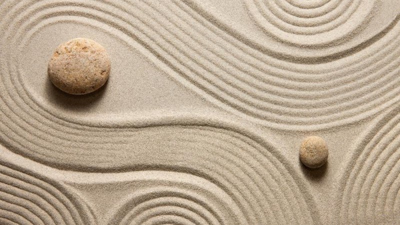 Zwei Steine liegen auf wellenförmig geharktem Sand, der an einen Zen-Garten erinnert. Die Linien umkreisen die Steine harmonisch., © AdobeStock_62532777_Olga Lyubkin-min Zwei Steine liegen auf wellenförmig geharktem Sand, der an einen Zen-Garten erinnert. Die Linien umkreisen die Steine harmonisch., © AdobeStock_62532777_Olga Lyubkin-min