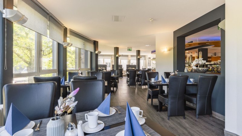 Moderner Fr&uuml;hst&uuml;cksbereich mit gedeckten Tischen, blauen Servietten und gro&szlig;en Fenstern, die viel Licht hereinlassen., &copy; Plaza INN Stuttgart-Filderstadt