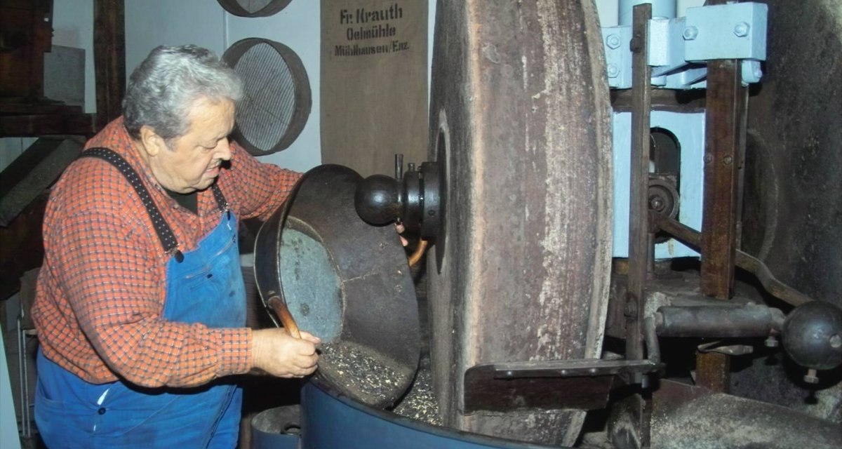 Ein Mann in blauer Latzhose arbeitet an einer alten Ölmühle mit großen Steinen in Illingen., © Kraichgau-Stromberg Tourismus e.V. Ein Mann in blauer Latzhose arbeitet an einer alten Ölmühle mit großen Steinen in Illingen., © Kraichgau-Stromberg Tourismus e.V.