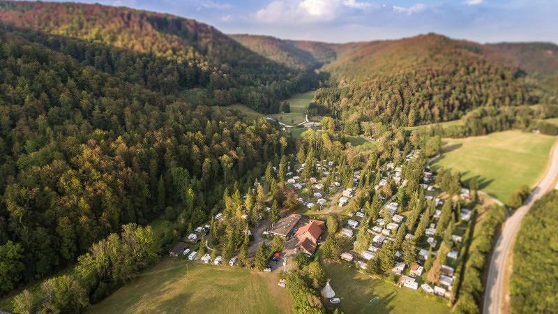 Luftaufnahme des Campingplatzes Pfählhof in einem bewaldeten Tal mit Wohnwagen und Zelten, umgeben von Hügeln und einer Straße., © Campingplatz Pfählhof