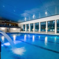 Ein Hallenbad mit blauem Wasser, großen Fenstern und einem Wasserstrahl. Die Decke ist blau, und es gibt eine Galerie im Hintergrund., © Brosch Fotografie / Stadt Wernau