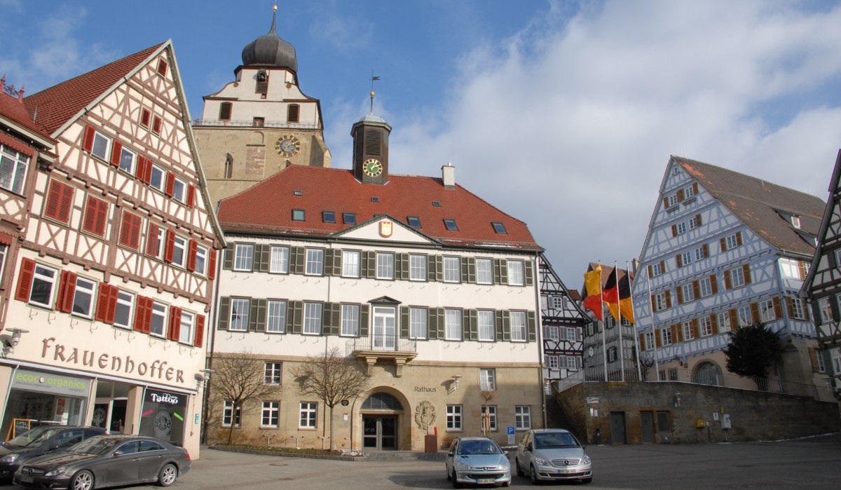 Der Marktplatz in Herrenberg zeigt Fachwerkh&auml;user und das Rathaus unter blauem Himmel. Autos parken vor den Geb&auml;uden., &copy; Natur.Nah. Sch&ouml;nbuch & Heckeng&auml;u