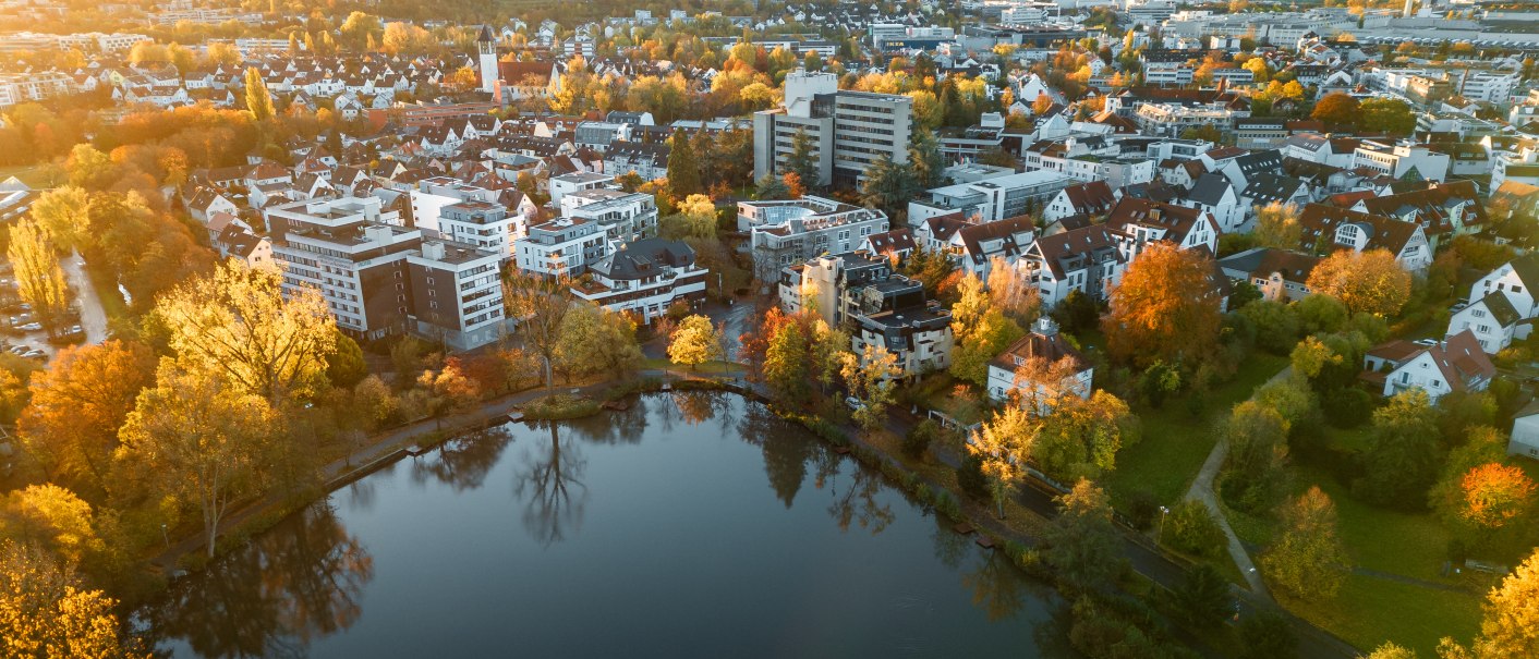 Luftaufnahme des Klostersees in Sindelfingen, umgeben von herbstlichen Bäumen und Wohngebäuden im Sonnenuntergang., © Christoph Partsch Luftaufnahme des Klostersees in Sindelfingen, umgeben von herbstlichen Bäumen und Wohngebäuden im Sonnenuntergang., © Christoph Partsch