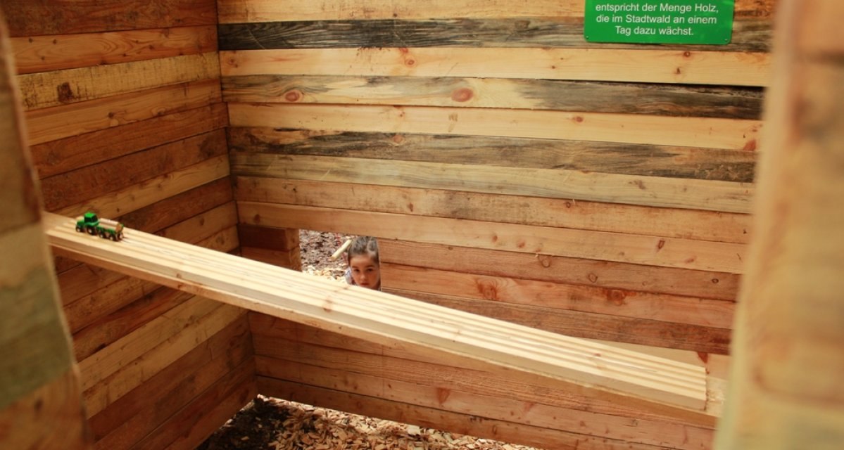 Innenansicht einer Holzkonstruktion mit Holzlatten und einem kleinen Fenster, durch das ein Kind schaut. Ein Spielzeugtraktor steht auf einem Balken., &copy; Amt f&uuml;r Forsten Landkreis B&ouml;blingen