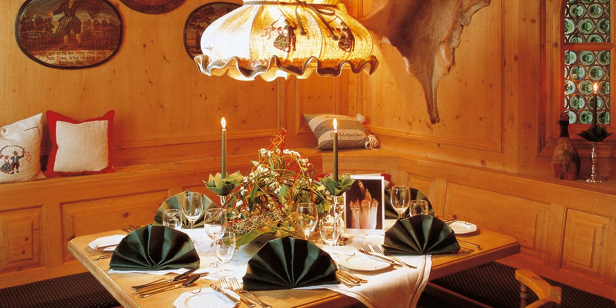 Ein rustikal gedeckter Tisch in einem Restaurant mit Holzverkleidung, Kerzen und grünen Servietten. Eine gemütliche Atmosphäre mit traditionellem Dekor., © © H-Hotels.com