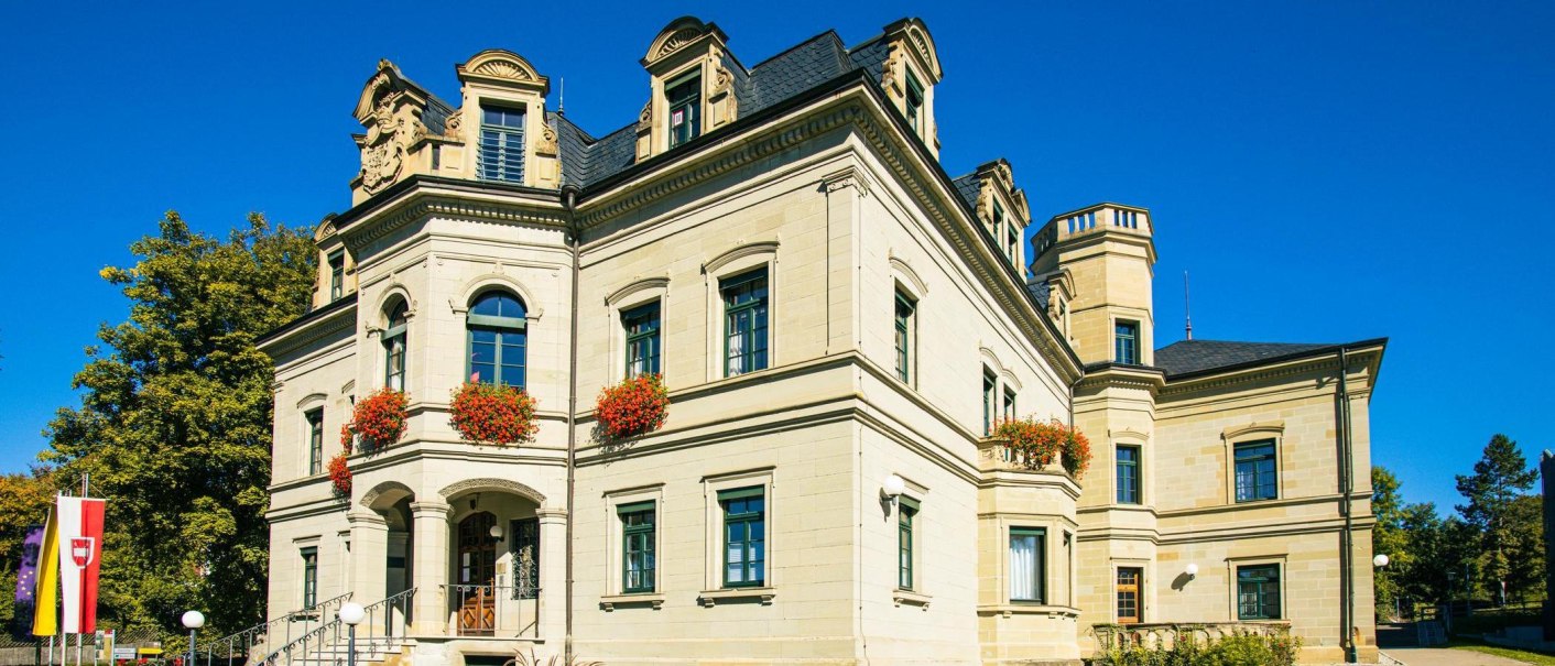 Das Neue Schloss in Gaildorf strahlt in der Sonne. Die Fassade ist mit Blumen geschmückt, und der Himmel ist klar und blau., © Stuttgart-Marketing GmbH, Sarah Schmid