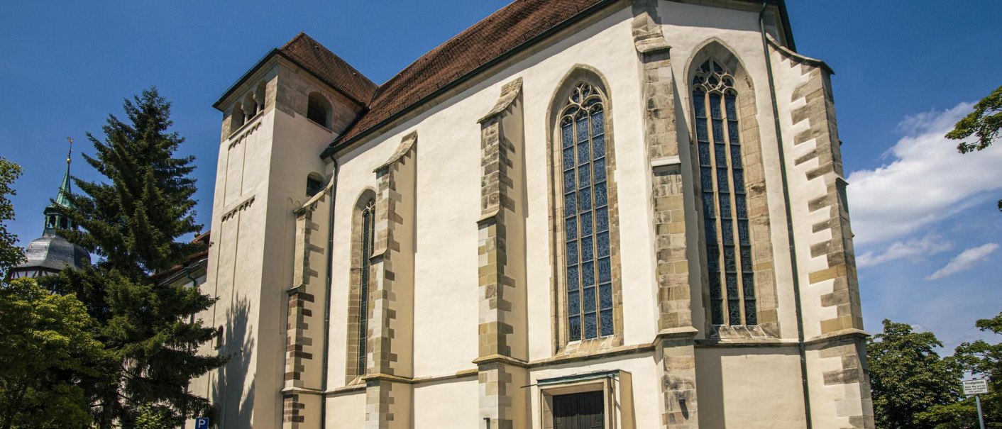 Kirche in Backnang mit gotischen Fenstern und Turm, umgeben von Bäumen und blauem Himmel., © Stuttgart-Marketing GmbH, Sarah Schmid