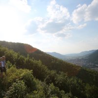Zwei Personen stehen auf einem bewaldeten Hügel und blicken ins Tal, wo eine Stadt liegt. Der Himmel ist leicht bewölkt und sonnig., © Bad Urach Tourismus