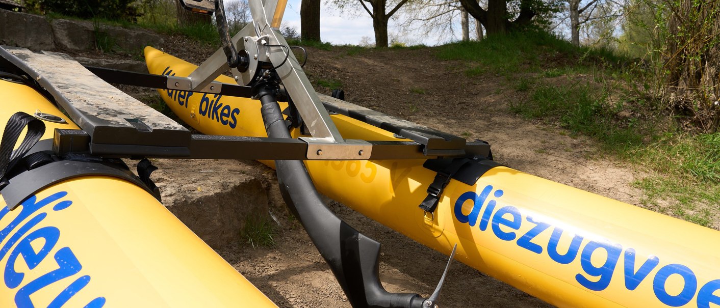 Gelbes Waterbike mit blauer Aufschrift und Metallrahmen auf einem sandigen Weg, umgeben von Bäumen., © Foto LKZ - Fotograf Andreas Becker