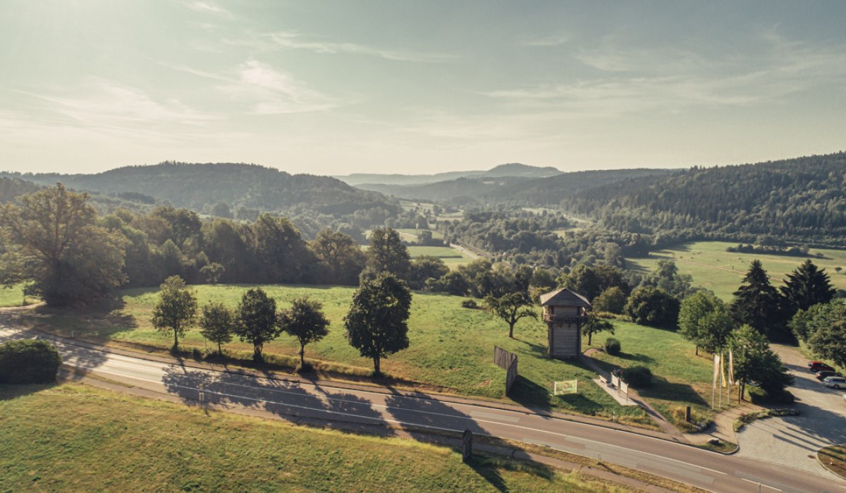 Blick auf eine grüne Landschaft mit einem Limesturm in Lorch, umgeben von Bäumen und Hügeln. Eine Straße verläuft im Vordergrund., © Tourismus Ostalb
