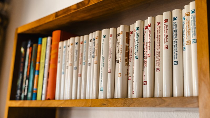 Ein Holzregal mit einer Reihe von B&uuml;chern in wei&szlig;en Einb&auml;nden, ordentlich nebeneinander aufgereiht., &copy; SMG Stuttgart Marketing GmbH - Sarah Schmid