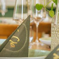 Ein elegant gedeckter Tisch mit gefalteten Servietten, Gläsern und dekorativen Elementen. Die Servietten tragen den Schriftzug 'Cla'., © FreCla Gastronomiebetriebe GmbH