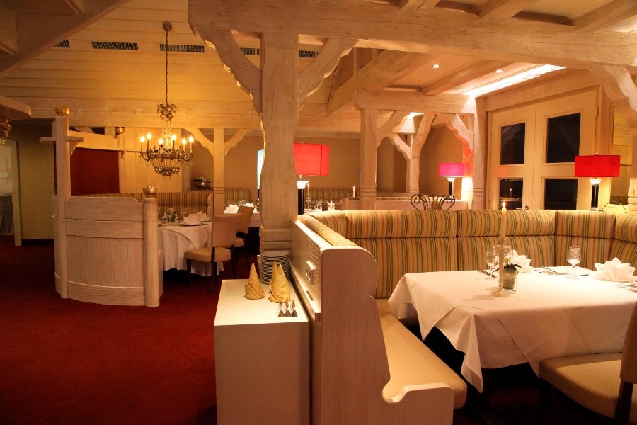 Elegantes Restaurant mit Holzbalken, roten Lampen und gedeckten Tischen auf rotem Teppichboden., © Hotel Fuchsen Elegantes Restaurant mit Holzbalken, roten Lampen und gedeckten Tischen auf rotem Teppichboden., © Hotel Fuchsen