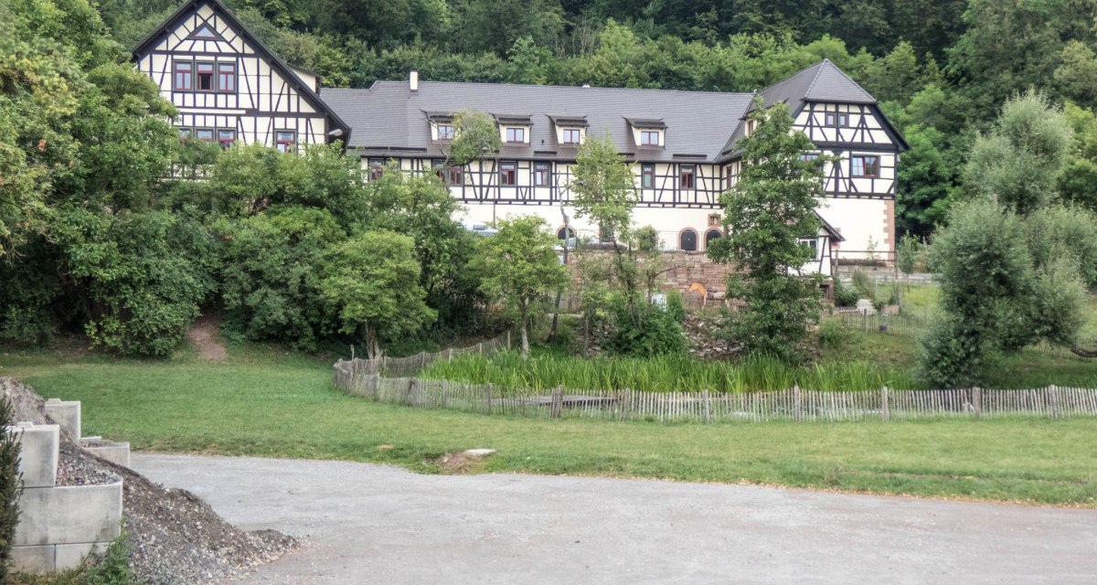 Ein gro&szlig;es Fachwerkhaus steht inmitten von B&auml;umen und gr&uuml;ner Landschaft. Ein Weg f&uuml;hrt an einer Wiese vorbei zum Haus., &copy; Natur.Nah. Sch&ouml;nbuch & Heckeng&auml;u