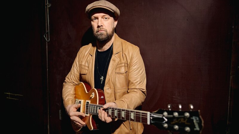 Eine Person mit Hut und Lederjacke steht mit einer E-Gitarre vor einem gelben Vorhang. Im Vordergrund ist ein Klavier zu sehen., © Scala Kultur Live gGmbH Eine Person mit Hut und Lederjacke steht mit einer E-Gitarre vor einem gelben Vorhang. Im Vordergrund ist ein Klavier zu sehen., © Scala Kultur Live gGmbH