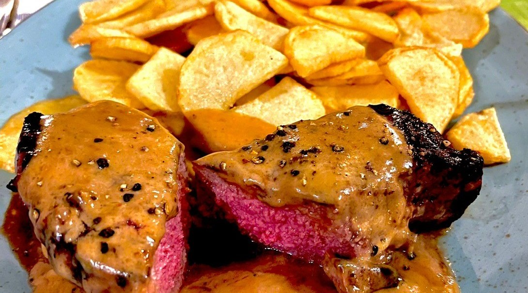 Ein Teller mit saftigem Steak in Pfeffersoße, serviert mit knusprigen Kartoffelchips auf einem blauen Teller., © Restaurant Neckaru, P. Kotaidis