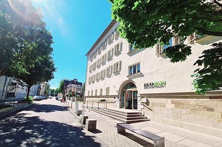 Ein Geb&auml;ude mit der Aufschrift 'BQQ INN' an einer sonnigen Stra&szlig;e, umgeben von B&auml;umen und klarem Himmel., &copy; ECOINN Hotel am Campus