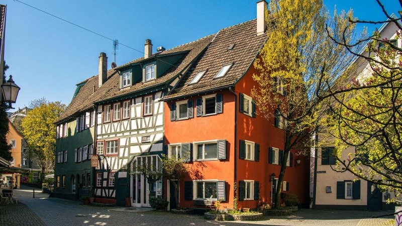 Fachwerkh&auml;user in der Altstadt von Schorndorf, umgeben von B&auml;umen und blauem Himmel. Die Geb&auml;ude sind bunt gestrichen und strahlen im Sonnenlicht., &copy; Stuttgart-Marketing GmbH, Sarah Schmid