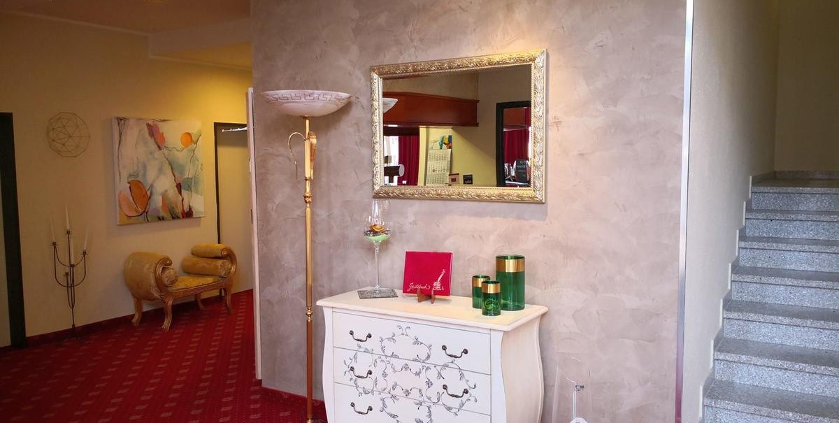 Elegante Lobby mit rotem Teppich, einer weißen Kommode, Spiegel, Stehlampe und dekorativen Elementen. Treppe rechts, Gemälde links., © Hotel Arcis Elegante Lobby mit rotem Teppich, einer weißen Kommode, Spiegel, Stehlampe und dekorativen Elementen. Treppe rechts, Gemälde links., © Hotel Arcis