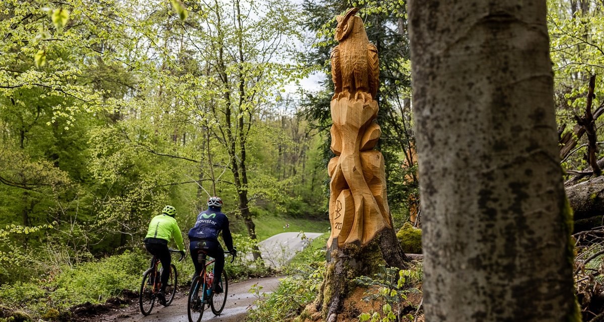 Zwei Radfahrer auf einem Waldweg neben einer großen Holzskulptur in einem grünen Wald bei Illingen-Schützingen., © Land der 1000 Hügel - Kraichgau-Stromberg Zwei Radfahrer auf einem Waldweg neben einer großen Holzskulptur in einem grünen Wald bei Illingen-Schützingen., © Land der 1000 Hügel - Kraichgau-Stromberg