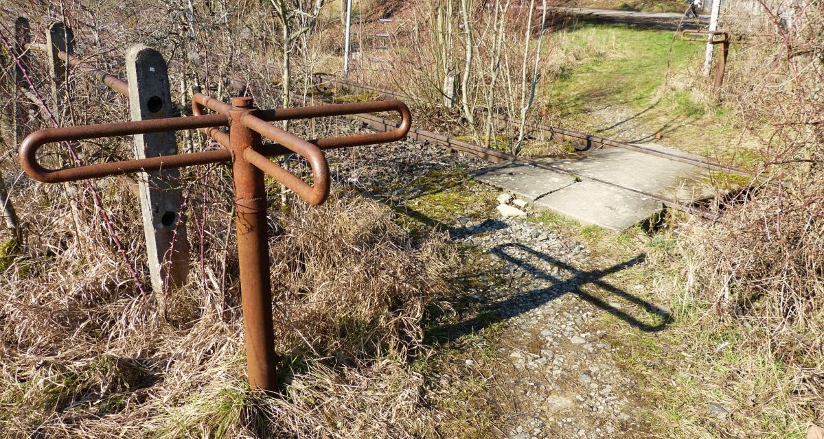 Ein rostiges Drehkreuz steht neben einem Pfad, der über die Schienen einer stillgelegten Bahnstrecke führt. Die Umgebung ist von Gras und Büschen bewachsen., © Natur.Nah. Schönbuch & Heckengäu Ein rostiges Drehkreuz steht neben einem Pfad, der über die Schienen einer stillgelegten Bahnstrecke führt. Die Umgebung ist von Gras und Büschen bewachsen., © Natur.Nah. Schönbuch & Heckengäu