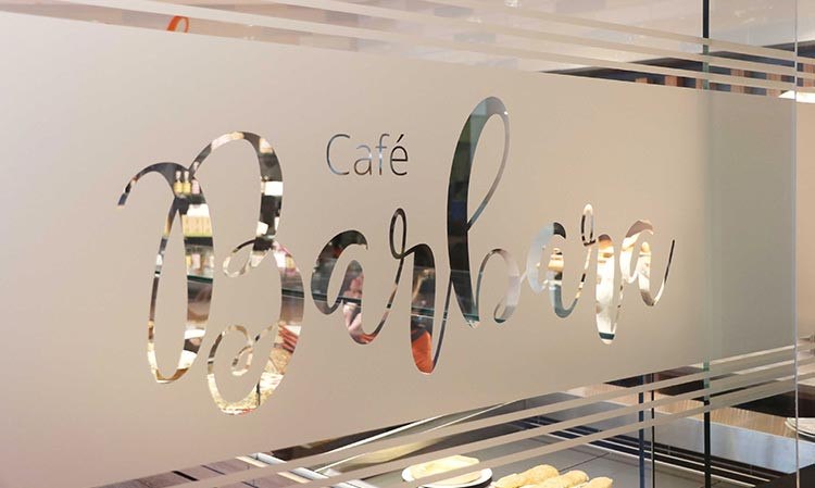 Eine Glaswand mit dem Schriftzug 'Café Barbara', durch die man ein Regal mit Backwaren sieht., © Biosphärenhotel Graf Eberhard