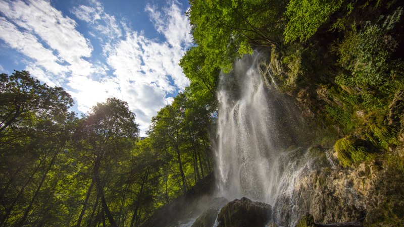 Der Uracher Wasserfall stürzt über Felsen, umgeben von dichtem Wald. Der Himmel ist blau mit weißen Wolken., © Bad Urach Tourismus Der Uracher Wasserfall stürzt über Felsen, umgeben von dichtem Wald. Der Himmel ist blau mit weißen Wolken., © Bad Urach Tourismus