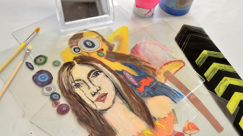 Ein gemaltes Portr&auml;t auf einer durchsichtigen Oberfl&auml;che, umgeben von Pinseln, Farben und dekorativen Elementen auf einem Tisch., &copy; Kunstschule Labyrinth