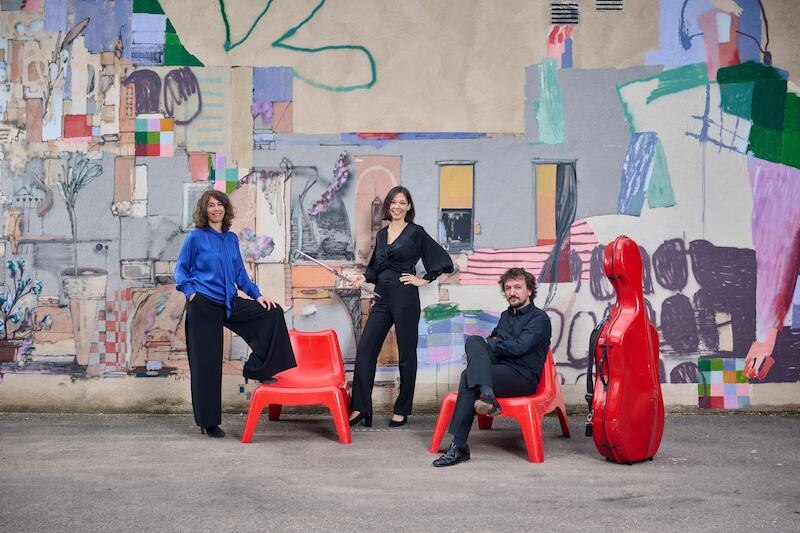 Drei Personen vor bunter Graffiti-Wand, zwei sitzen auf roten Stühlen, eine steht. Ein rotes Cello-Etui ist zu sehen., © Stadt Leonberg - Amt für Kultur und Sport