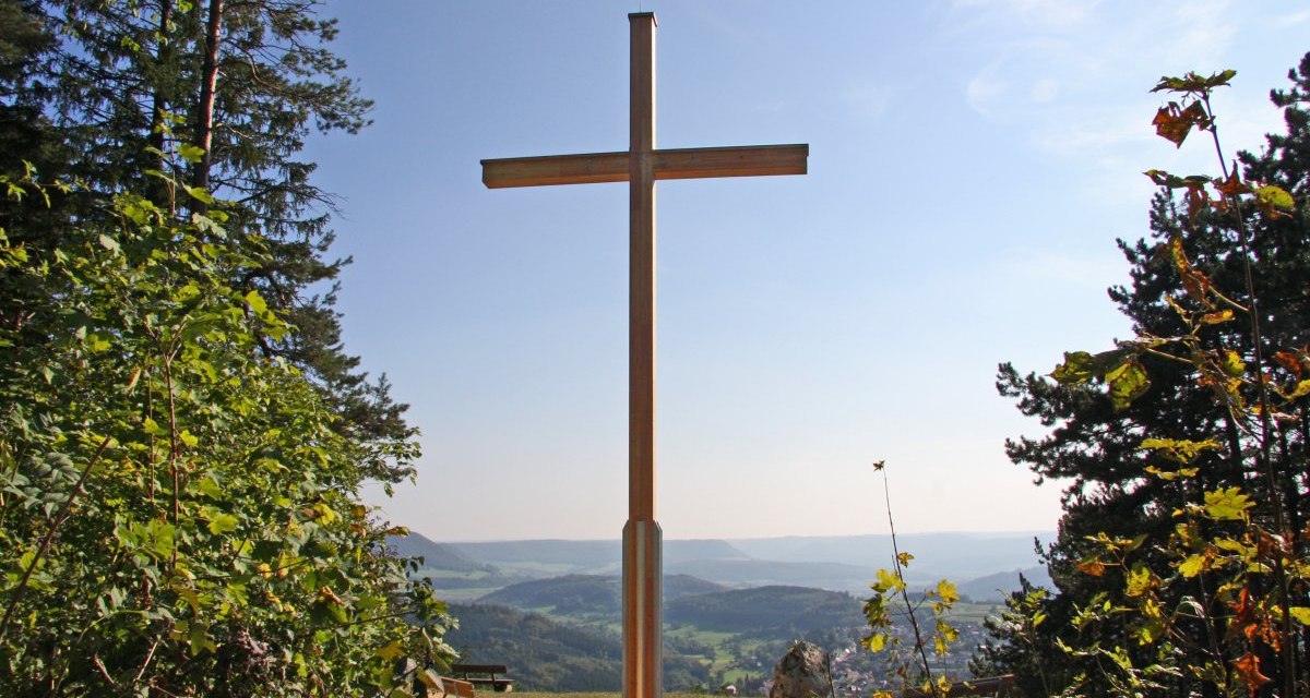 Ein gro&szlig;es Holzkreuz auf einem H&uuml;gel mit Blick auf eine weite Landschaft, umgeben von B&auml;umen und B&auml;nken., &copy; Foto: Frieder Kopper