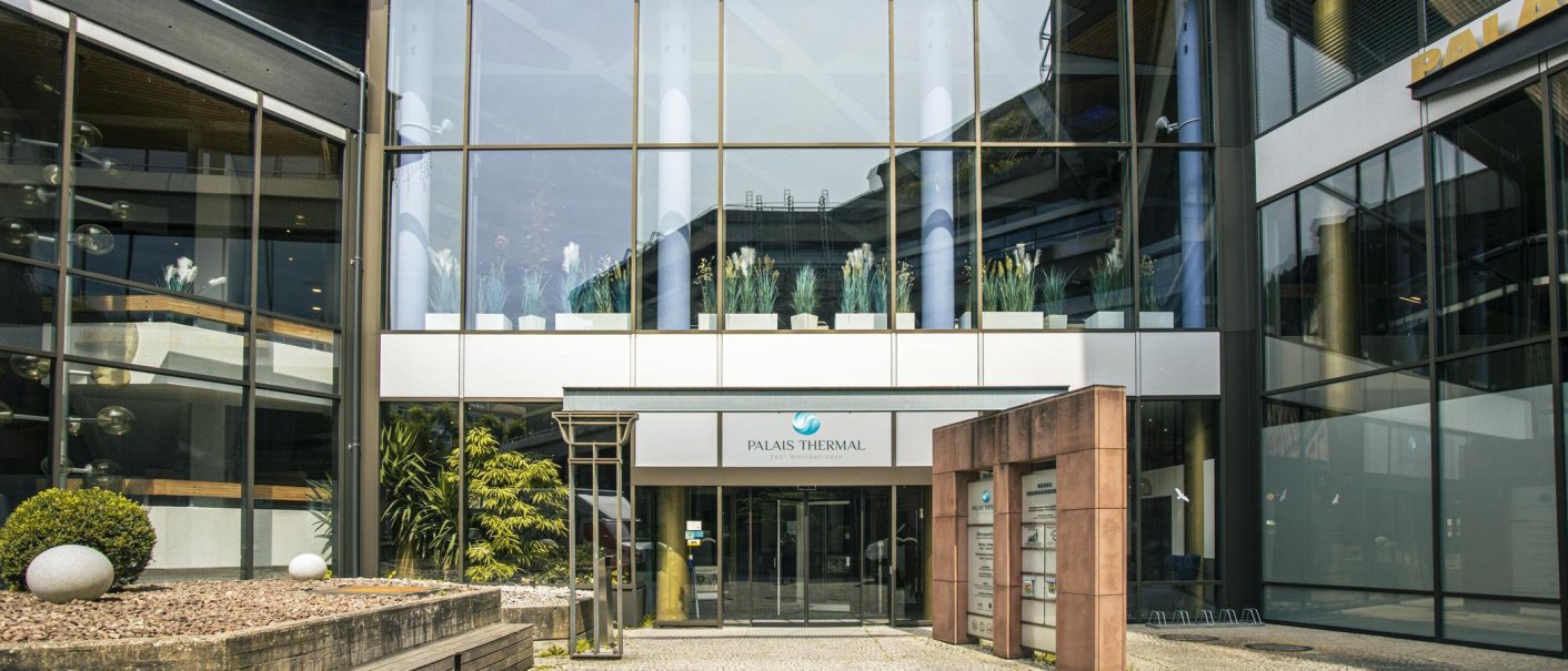 Eingang des Palais Thermal in Bad Wildbad, moderne Glasfassade mit Pflanzen dekoriert. Der Schriftzug 'Palais Thermal' ist über dem Eingang sichtbar., © Stuttgart-Marketing GmbH, Sarah Schmid Eingang des Palais Thermal in Bad Wildbad, moderne Glasfassade mit Pflanzen dekoriert. Der Schriftzug 'Palais Thermal' ist über dem Eingang sichtbar., © Stuttgart-Marketing GmbH, Sarah Schmid