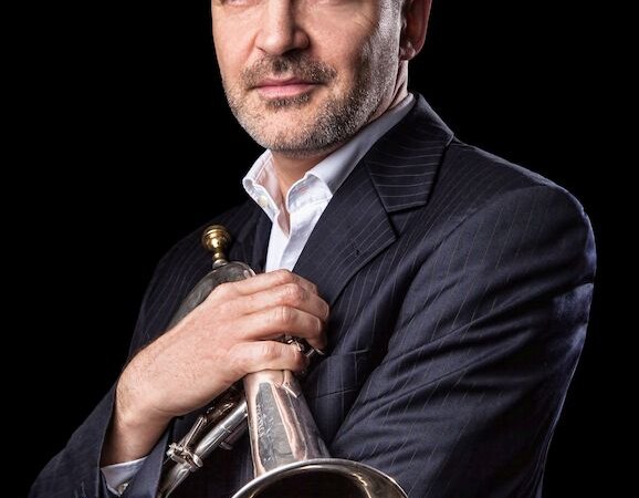 Ein Mann im Anzug h&auml;lt eine Trompete und blickt selbstbewusst in die Kamera. Der Hintergrund ist schwarz, was den Fokus auf die Person lenkt., &copy; Stadt B&ouml;blingen - Amt f&uuml;r Kultur