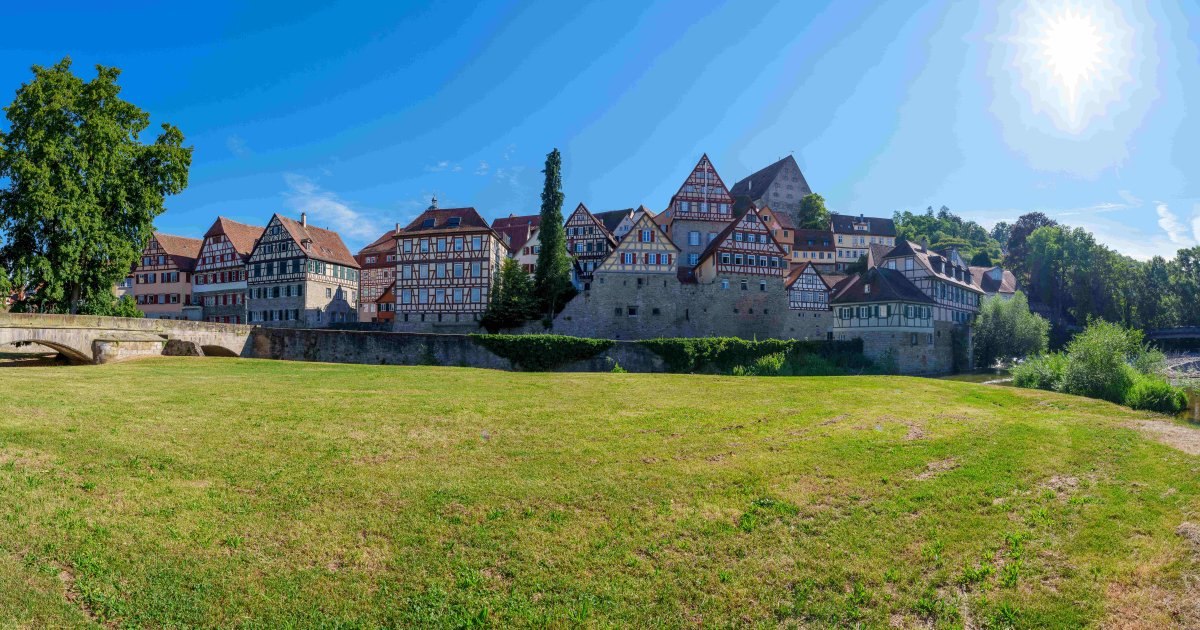 Panorama von Schw&auml;bisch Hall mit historischen Fachwerkh&auml;usern, einer Steinbr&uuml;cke und einer gr&uuml;nen Wiese unter blauem Himmel., &copy; Michael K&uuml;hneisen