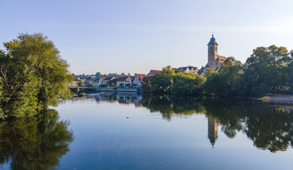 Blick über den Neckar auf eine Kirche und Häuser, umgeben von Bäumen, die sich im Wasser spiegeln., © Stadt Nürtingen Blick über den Neckar auf eine Kirche und Häuser, umgeben von Bäumen, die sich im Wasser spiegeln., © Stadt Nürtingen