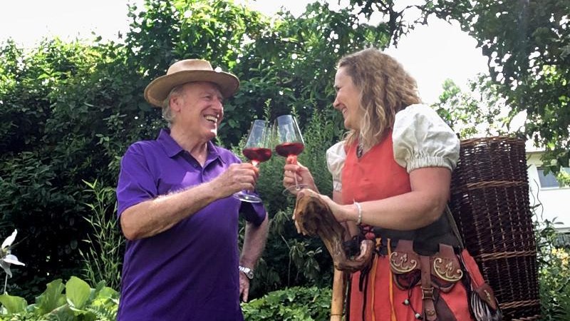 Ein Mann und eine Frau sto&szlig;en im Garten mit Rotweingl&auml;sern an. Die Frau tr&auml;gt ein traditionelles Kost&uuml;m und einen Wanderstock., &copy; Foto: G&uuml;nther Schuster