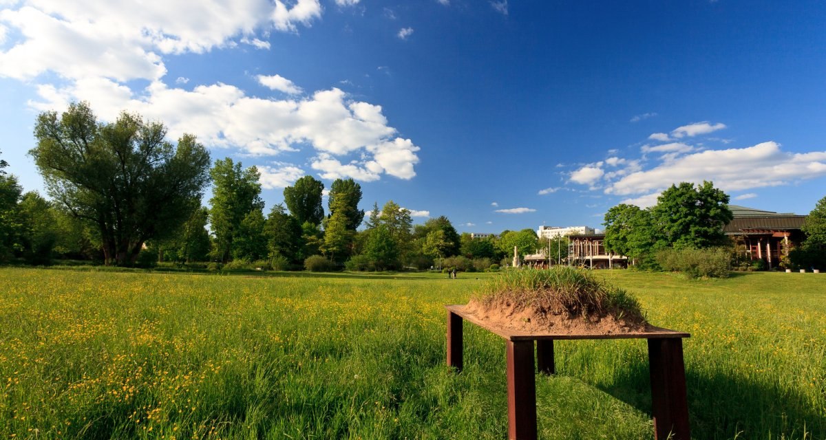 Ein Stahltisch mit Erdschollen steht auf einer grünen Wiese. Im Hintergrund sind Bäume und ein Gebäude zu sehen, der Himmel ist blau mit Wolken., © Remstal Tourismus e.V. Ein Stahltisch mit Erdschollen steht auf einer grünen Wiese. Im Hintergrund sind Bäume und ein Gebäude zu sehen, der Himmel ist blau mit Wolken., © Remstal Tourismus e.V.