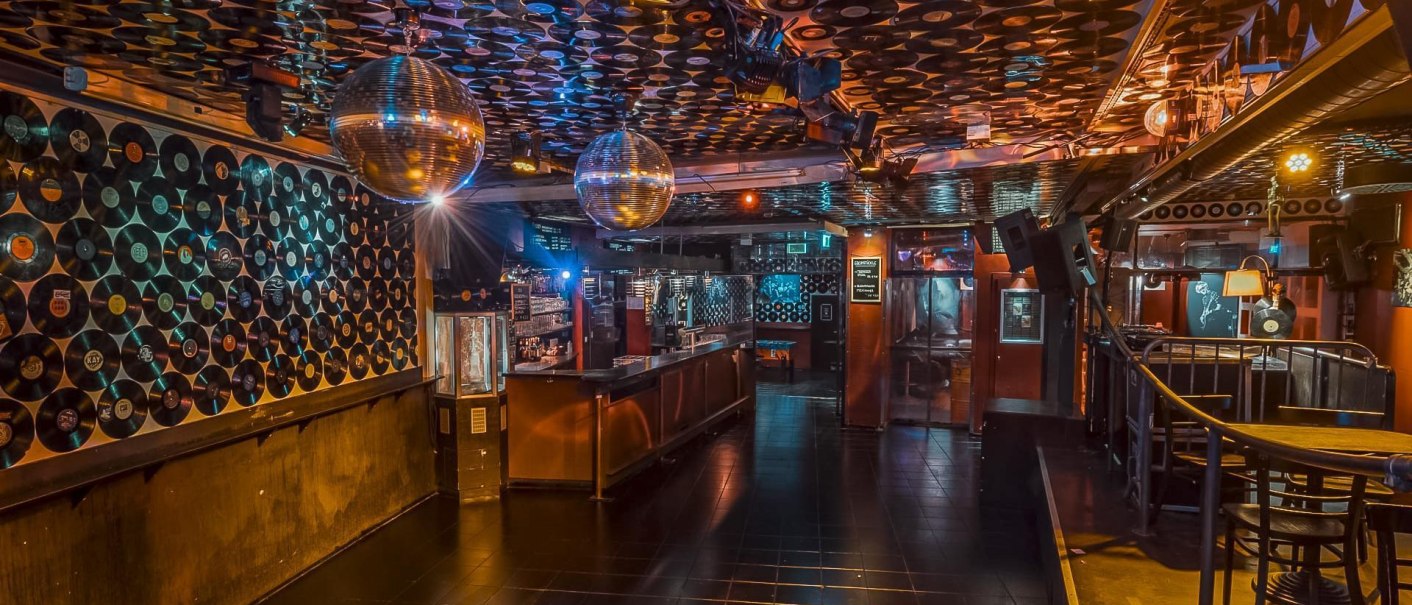 Club mit Schallplatten an Wänden und Decke, Discokugeln und Bar. Stimmungsvolle Beleuchtung und leere Tanzfläche., © Goldmarks, Stuttgart
