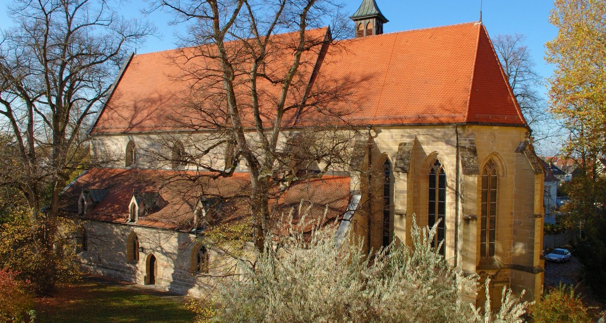 Die Schlosskirche in Winnenden mit rotem Ziegeldach und gotischen Fenstern, umgeben von herbstlichen Bäumen unter blauem Himmel., © SWT